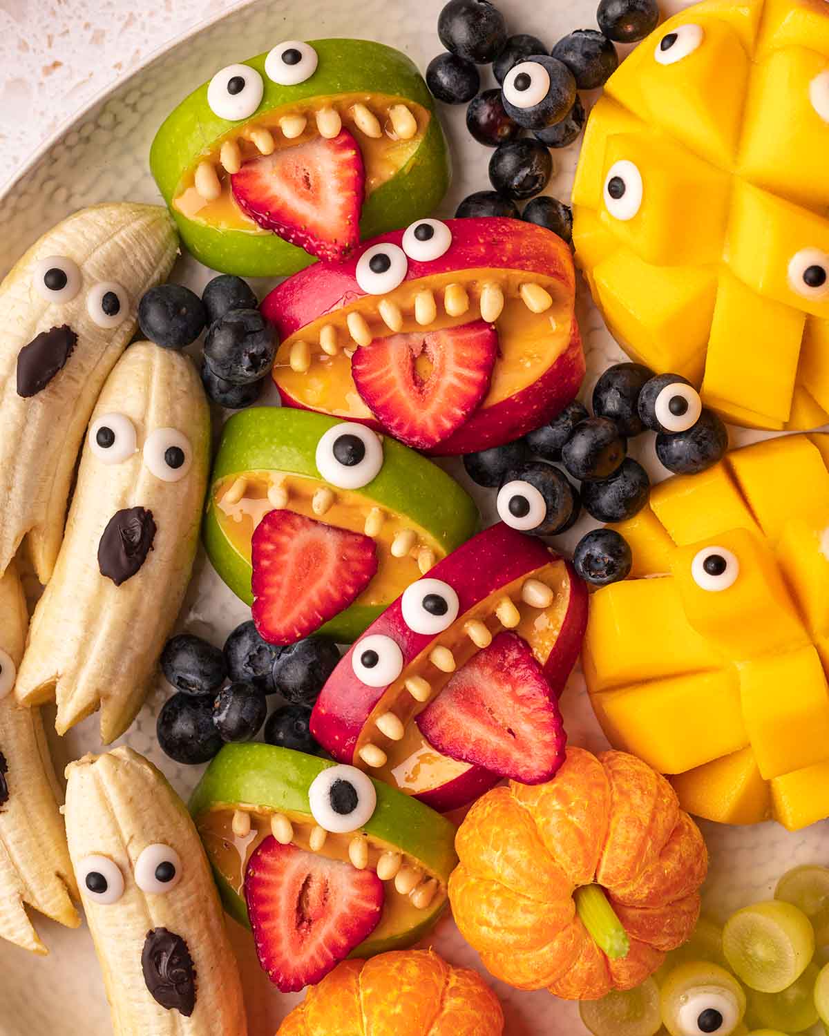 Close up of apple monsters, banana ghosts, mandarin pumpkins and blueberries on the Halloween snack platter.