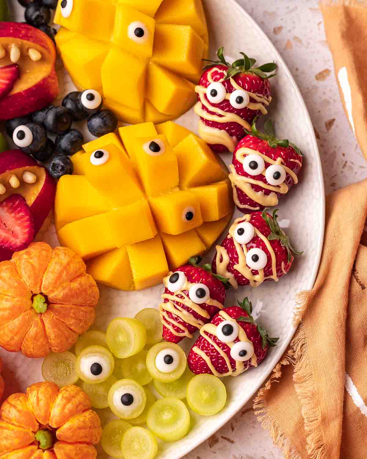 Close up of the spooky strawberry mummies, grape eyes and mango on the platter.