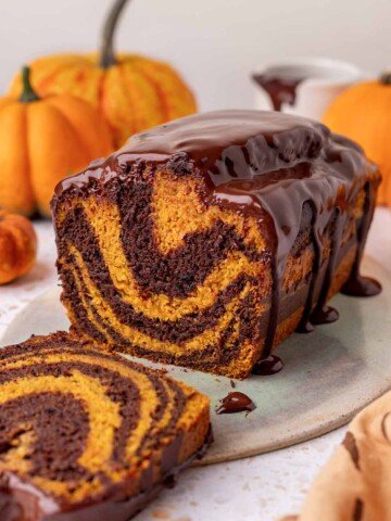 Pumpkin marble cake on serving plate with slice cut out showing contrasting orange and dark brown layers.