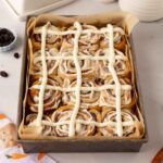Cinnamon rolls in baking tray with a cross pattern drawn on top just like hot cross buns.