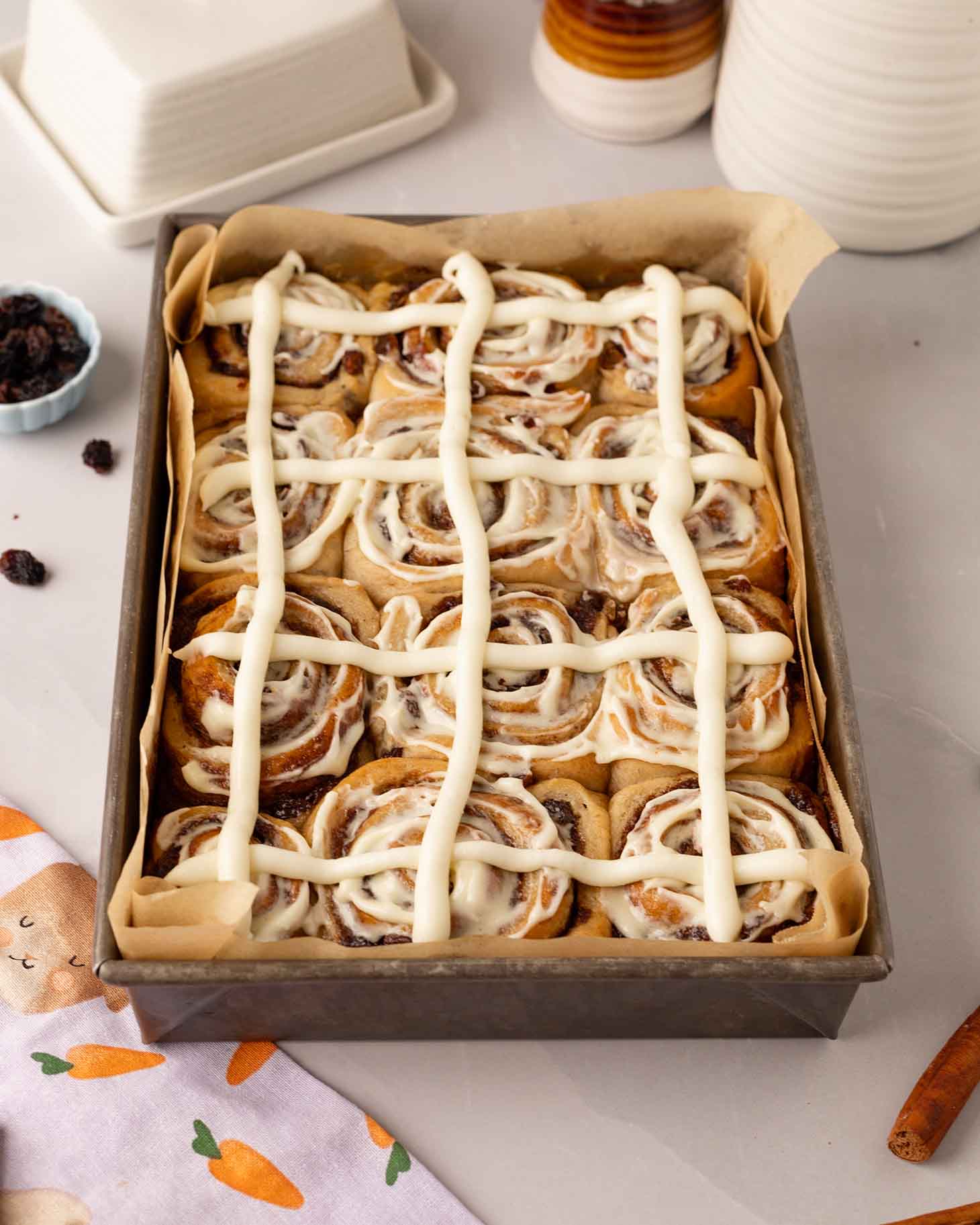 Cinnamon rolls in baking tray with a cross pattern drawn on top just like hot cross buns.