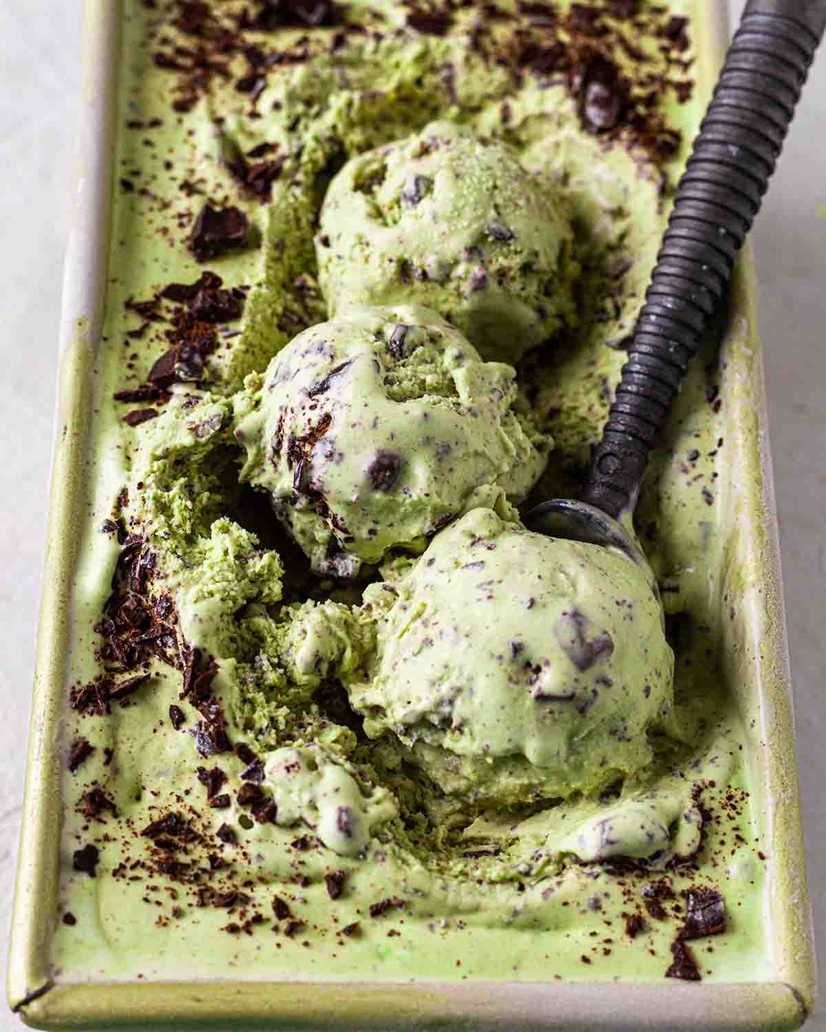 Side close up of melting mint chocolate chip ice cream in loaf pan.