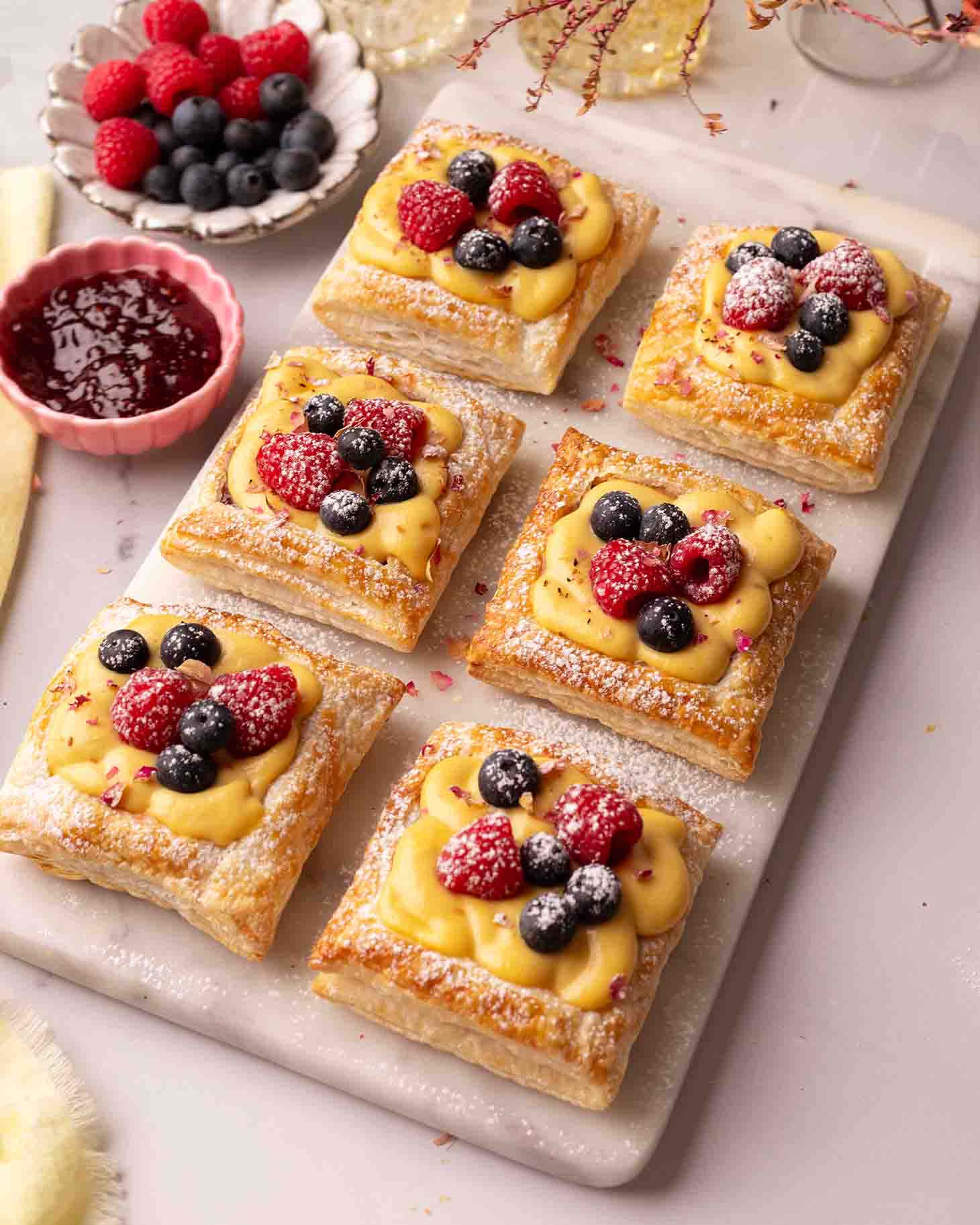 Puff pastry squares filled with custard and topped with fresh berries on a serving platter.