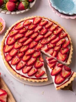 Tart with a shortcrust pastry, border of jam, cream filling and topped with sliced strawberries arranged in a petal pattern.