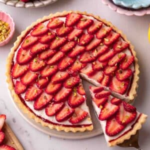 Tart with a shortcrust pastry, border of jam, cream filling and topped with sliced strawberries arranged in a petal pattern.