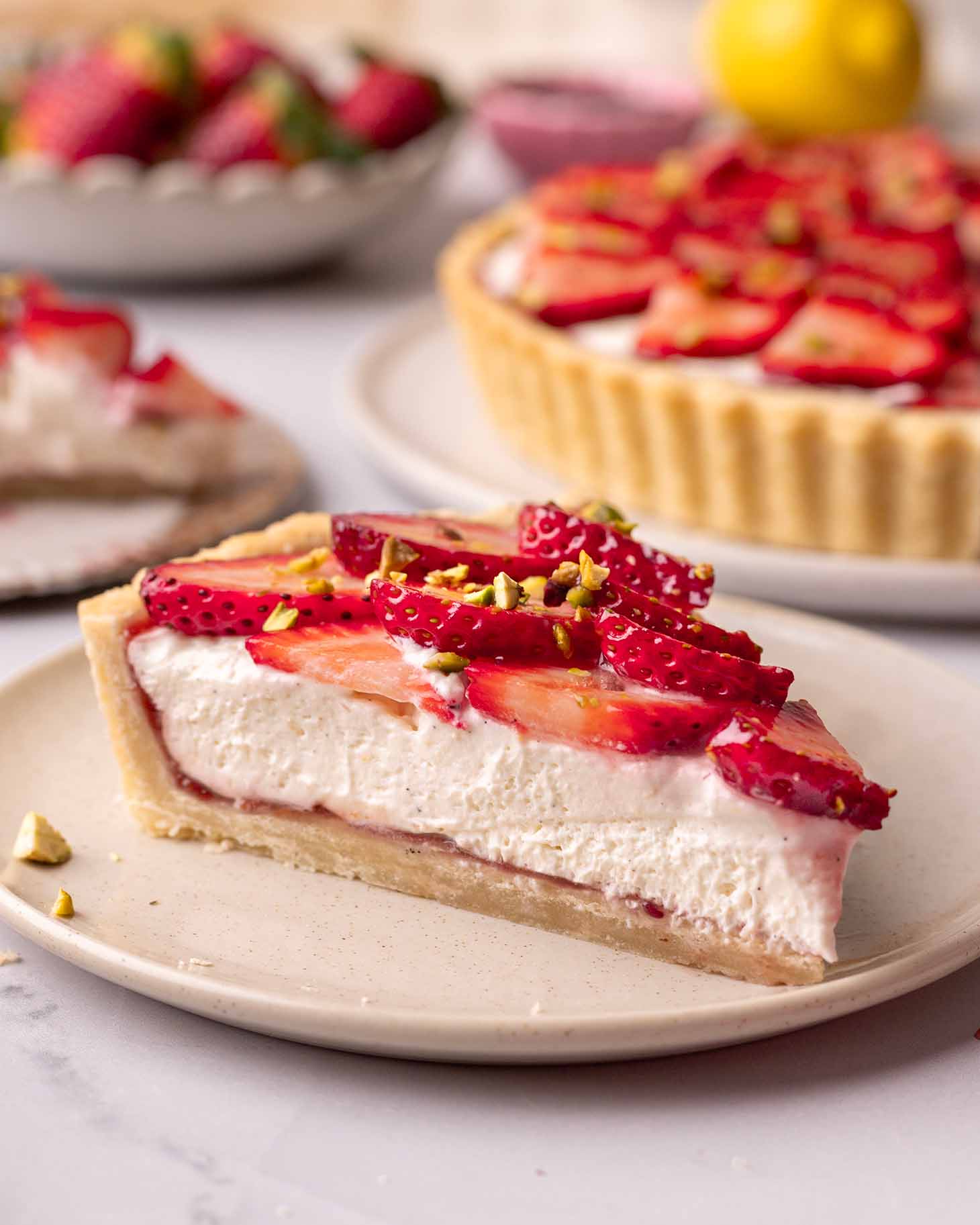 Close up of a slice of strawberry tart showing a fluffy cream, layer of jam and fresh strawberry topping.