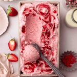 Strawberry ice cream with lots of strawberry swirls in a loaf pan with an ice cream scoop.