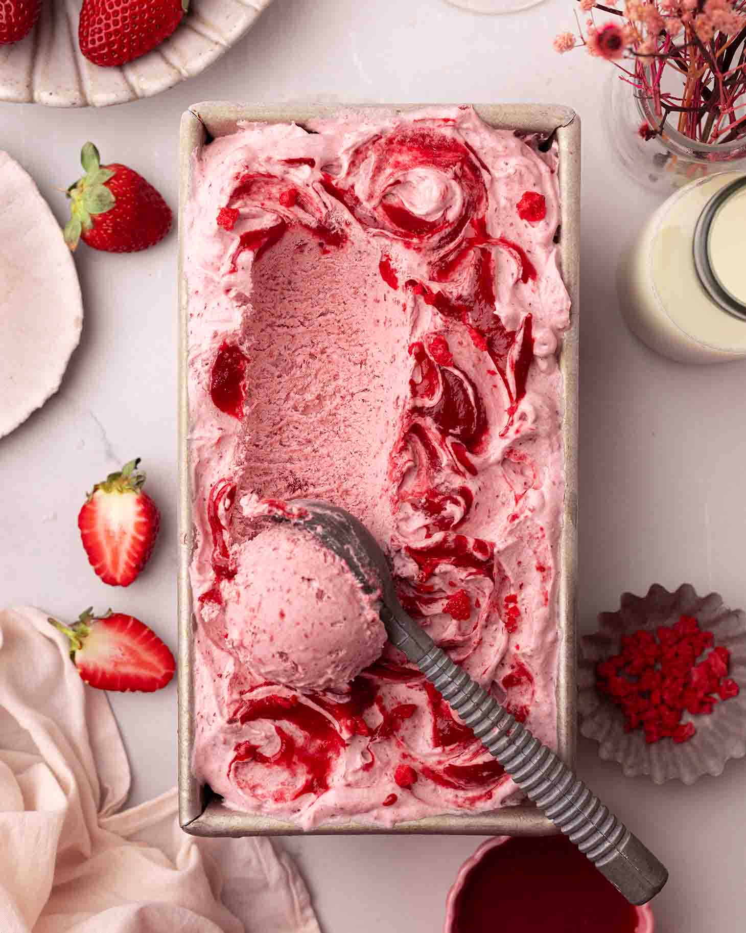 Strawberry ice cream with lots of strawberry swirls in a loaf pan with an ice cream scoop.