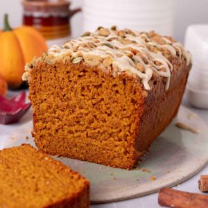Loaf of pumpkin bread on plate with slice cut off showing texture of the bread.