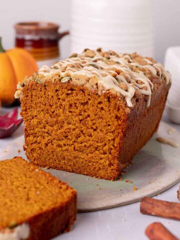 Loaf of pumpkin bread on plate with slice cut off showing texture of the bread.