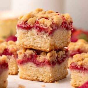 Stack of two cake squares, each with layers of a golden cake, jammy strawberries and crumb topping.