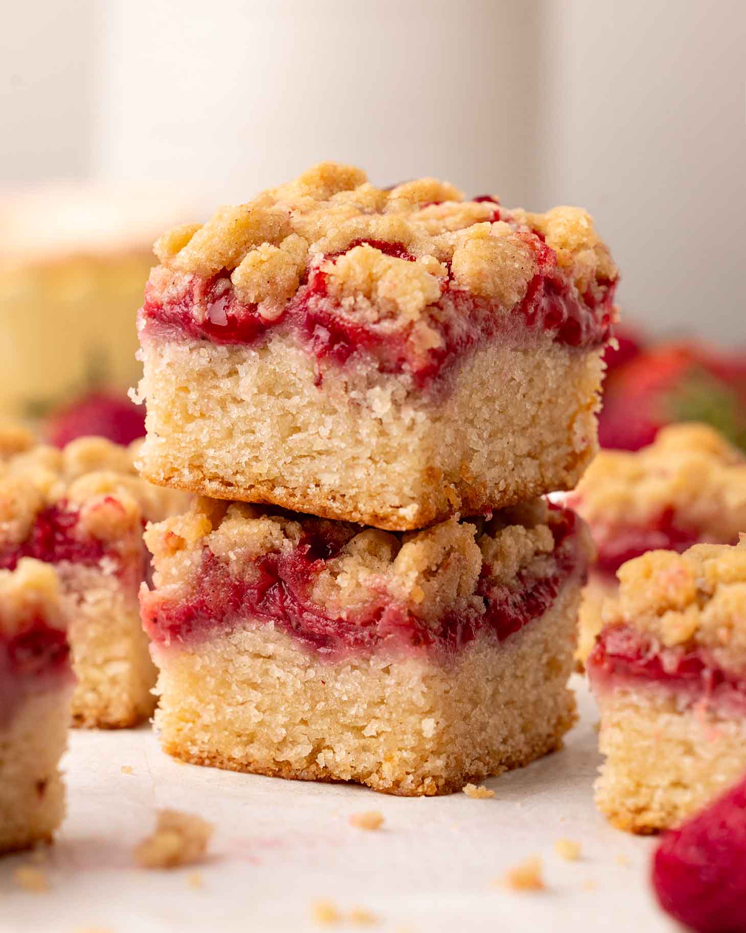 Stack of two cake squares, each with layers of a golden cake, jammy strawberries and crumb topping.