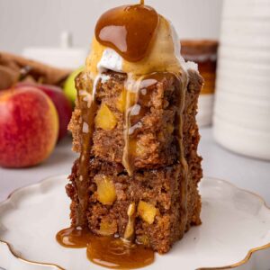 Stack of two squares of apple sticky toffee pudding, with a scoop of ice cream and toffee sauce poured on top.