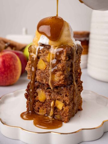 Stack of two squares of apple sticky toffee pudding, with a scoop of ice cream and toffee sauce poured on top.