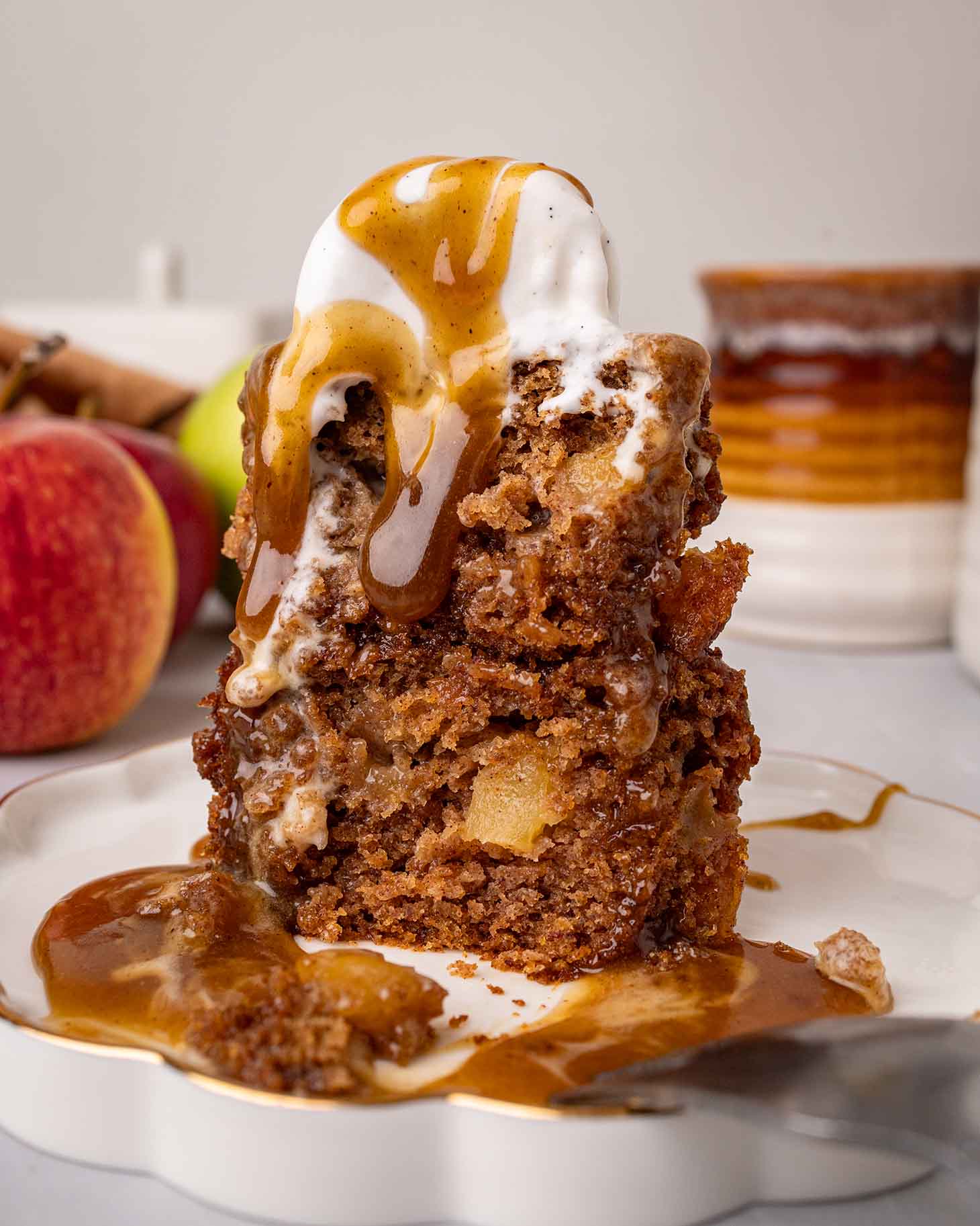 Stack of two apple sticky toffee pudding with ice cream and sauce. Bite taken out of pudding revealing golden and fluffy texture.