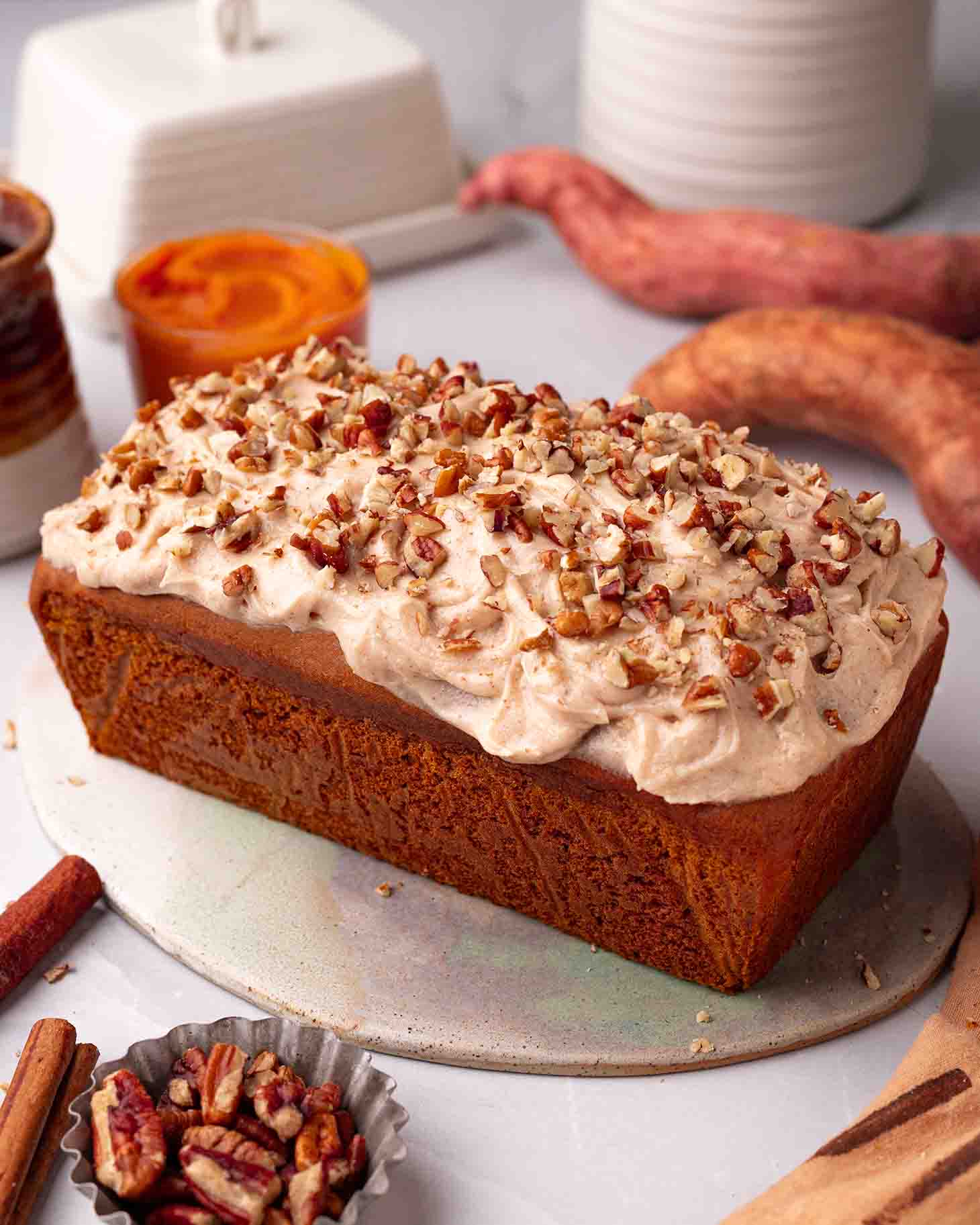 Whole sweet potato bread topped with cinnamon cream cheese frosting and pecans sprinkled on top.