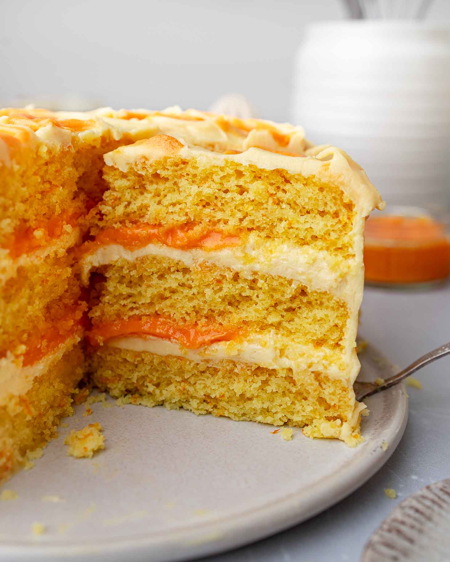 Slice of three-layered orange cake revealing fluffy cake layers, orange-flavored buttercream and orange curd.