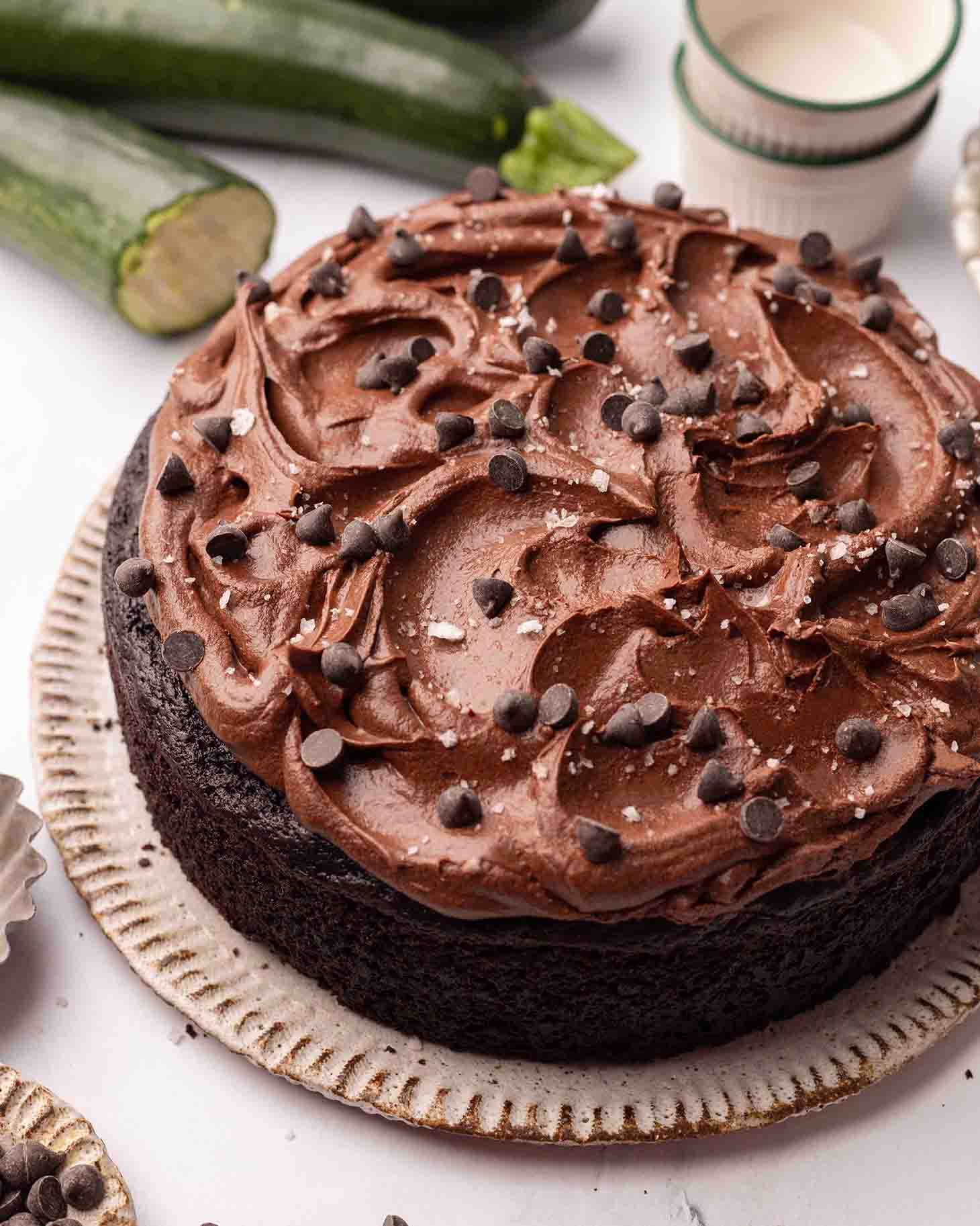 Cake on plate topped with chocolate ganache frosting, chocolate chips and flaky salt.
