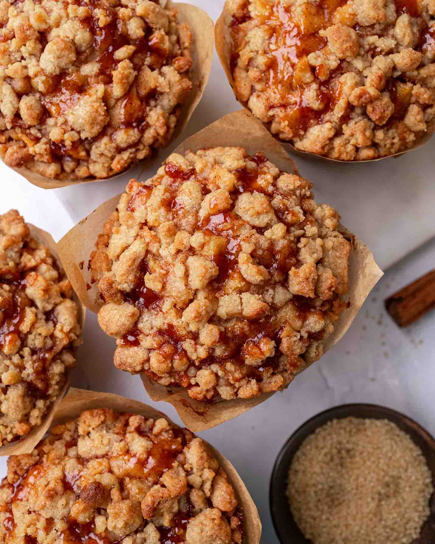 Overhead image of several muffins, showing the oozy gooey apple filling and abundant crumble.