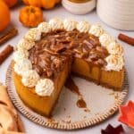 Vegan pumpkin cheesecake with a few slices removed to show creamy cheesecake filling. Cheesecake is topped with pecan caramel sauce and whipped cream.