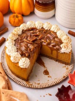 Vegan pumpkin cheesecake with a few slices removed to show creamy cheesecake filling. Cheesecake is topped with pecan caramel sauce and whipped cream.